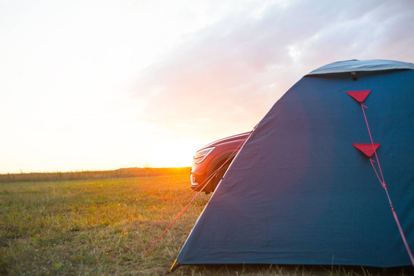 A blue tent next to a car on a grassy field at sunset.