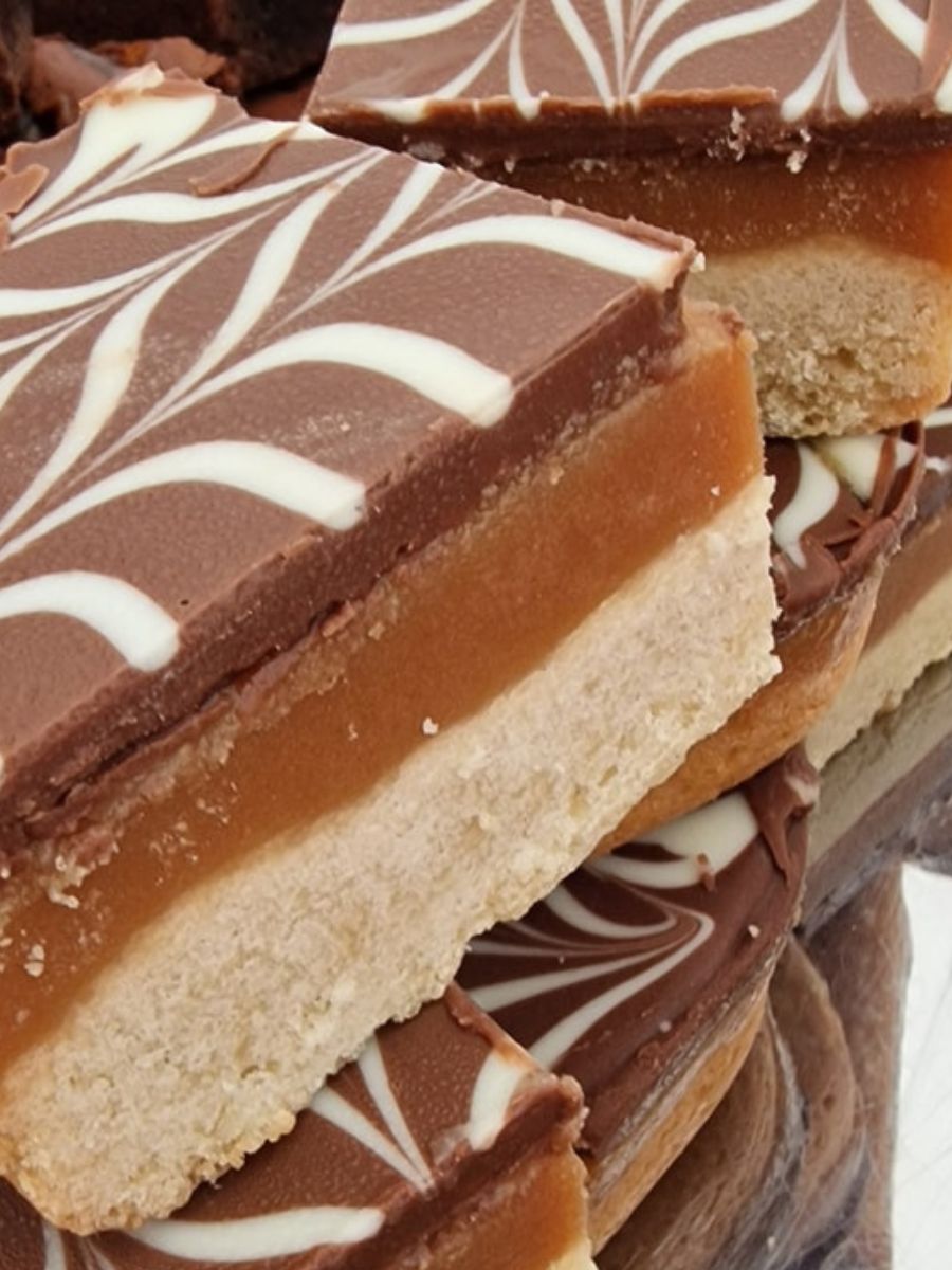 Close-up of layered dessert bars with a shortbread base, caramel middle layer, and chocolate topping decorated with a white swirl pattern.