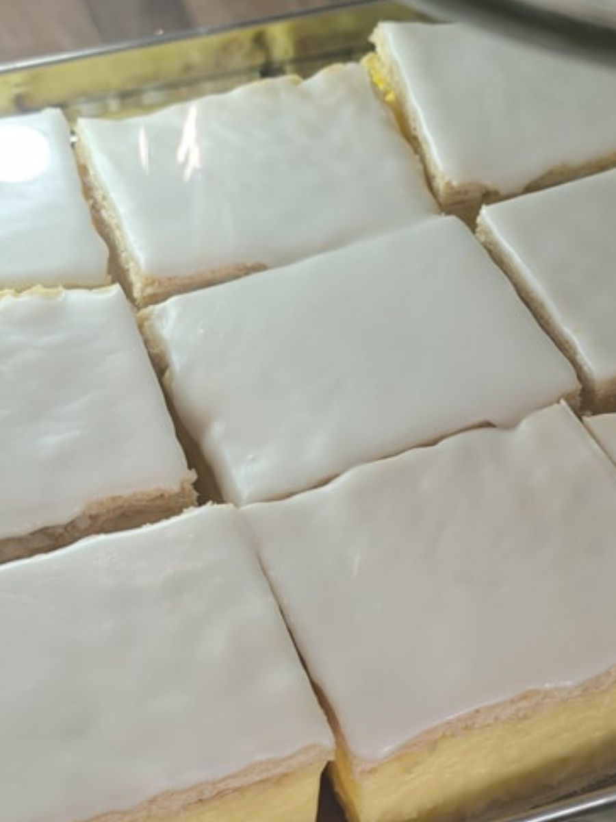 Nine square pieces of custard slices with smooth white icing, arranged in a metal tray.