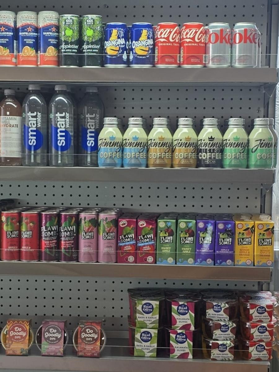 Shelves stocked with various canned and bottled drinks, including water, sodas, coffee, flavored drinks, and yogurt, organised in rows in a store display.