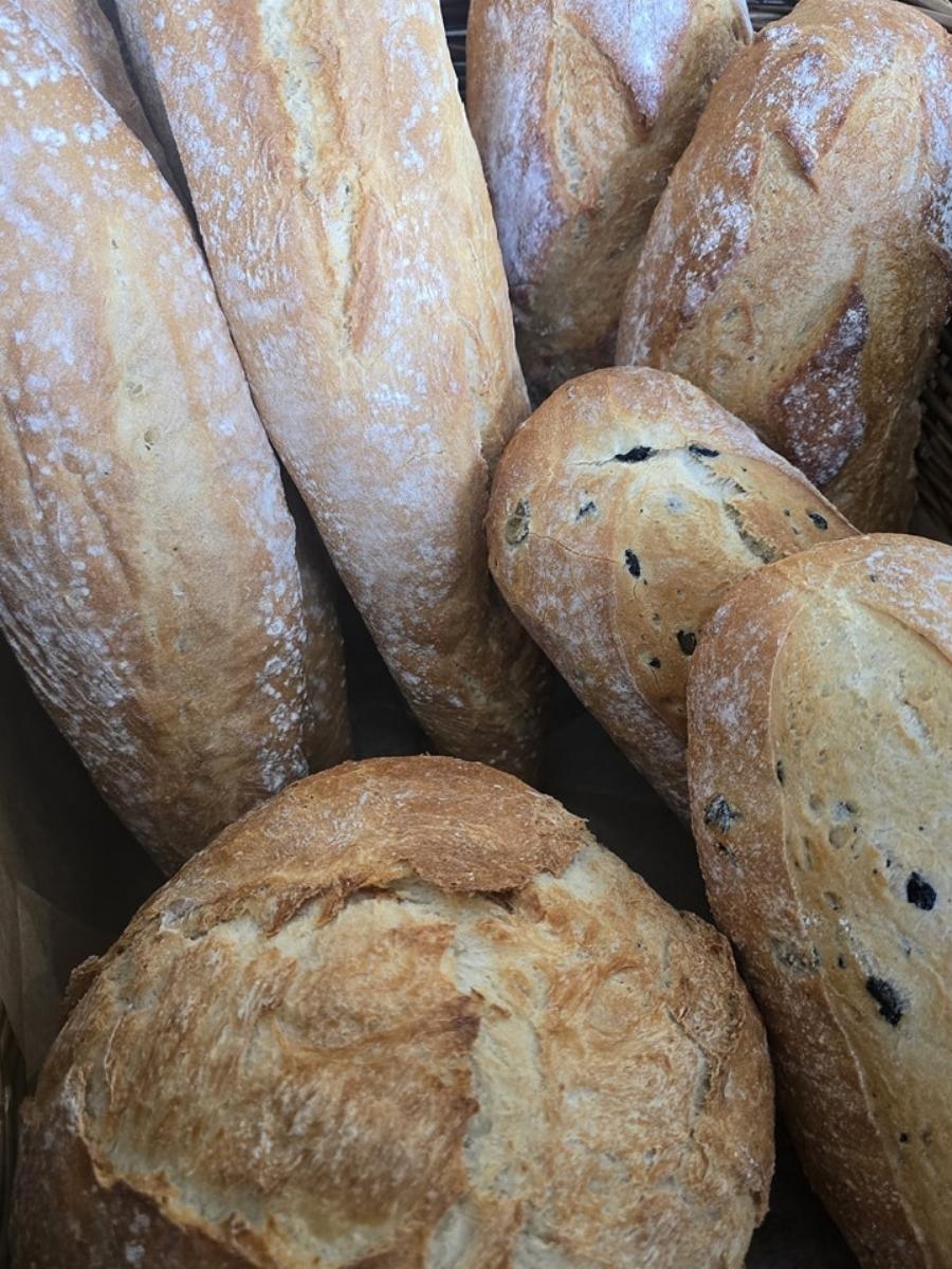 Assorted loaves of crusty bread, including round and long baguette-style shapes, with some containing visible dark inclusions, displayed in a basket.