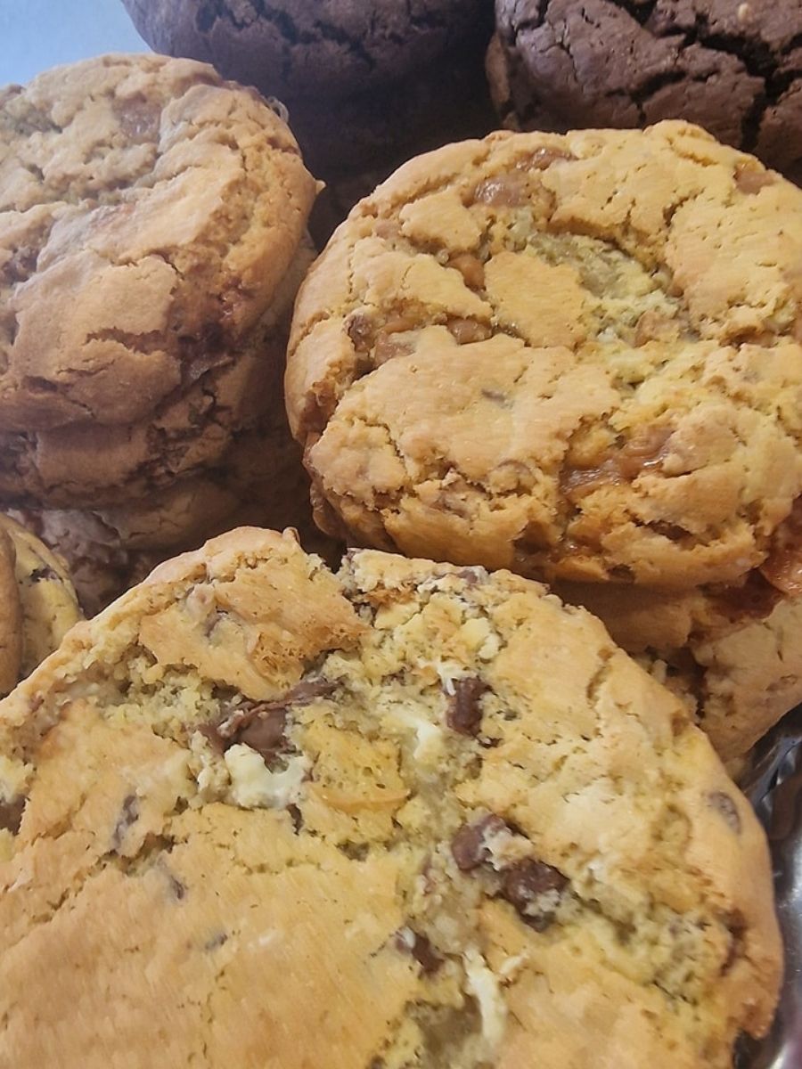 A close-up of several large, thick chocolate chip cookies, stacked together with visible chocolate chunks.