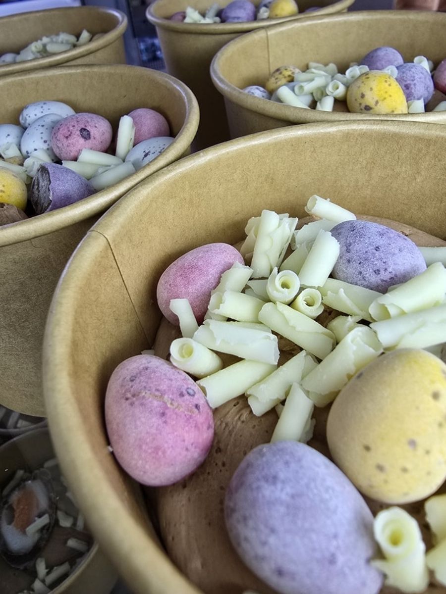 Several brown paper bowls filled with pastel-coloured candy mini-eggs and white chocolate curls.