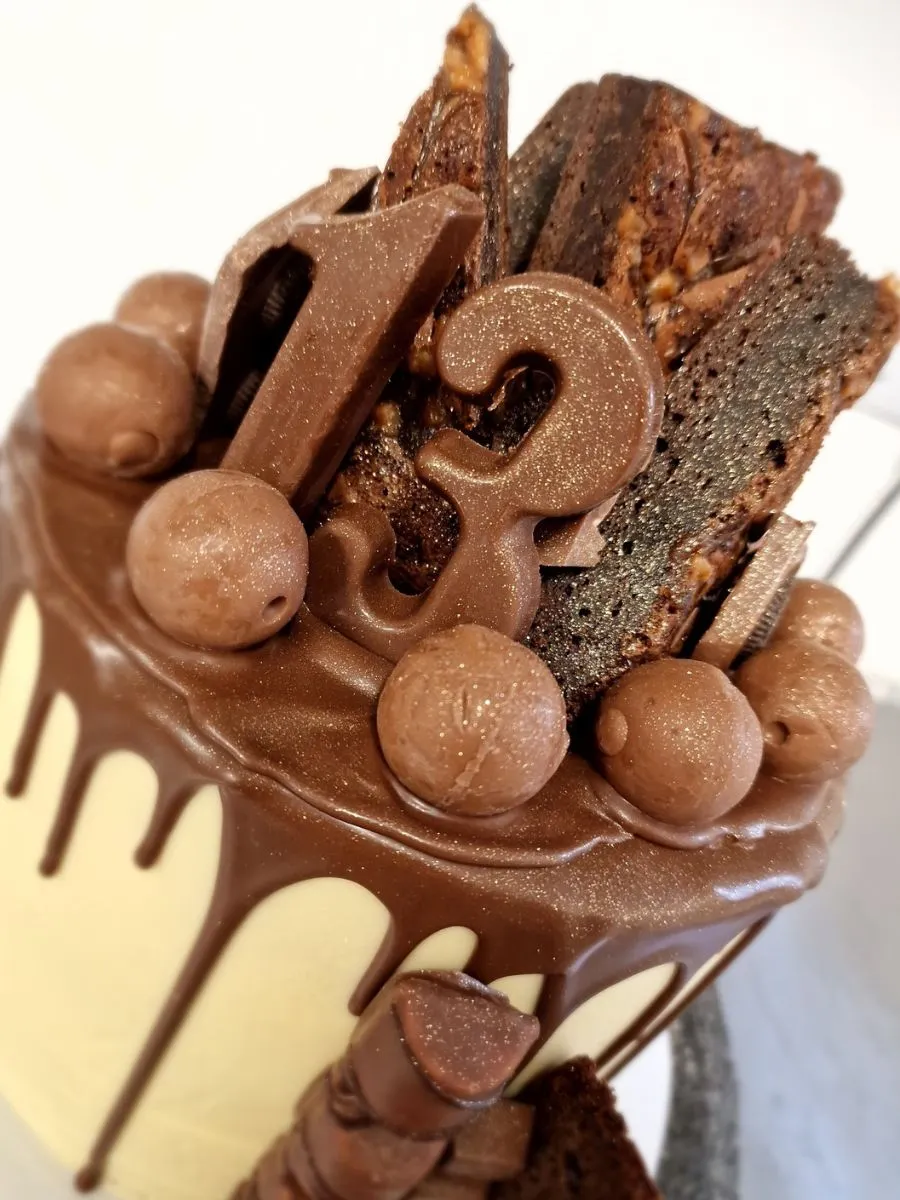 A cake decorated with chocolate drip, chocolate balls, brownies, and chocolate numbers forming "13" on top.
