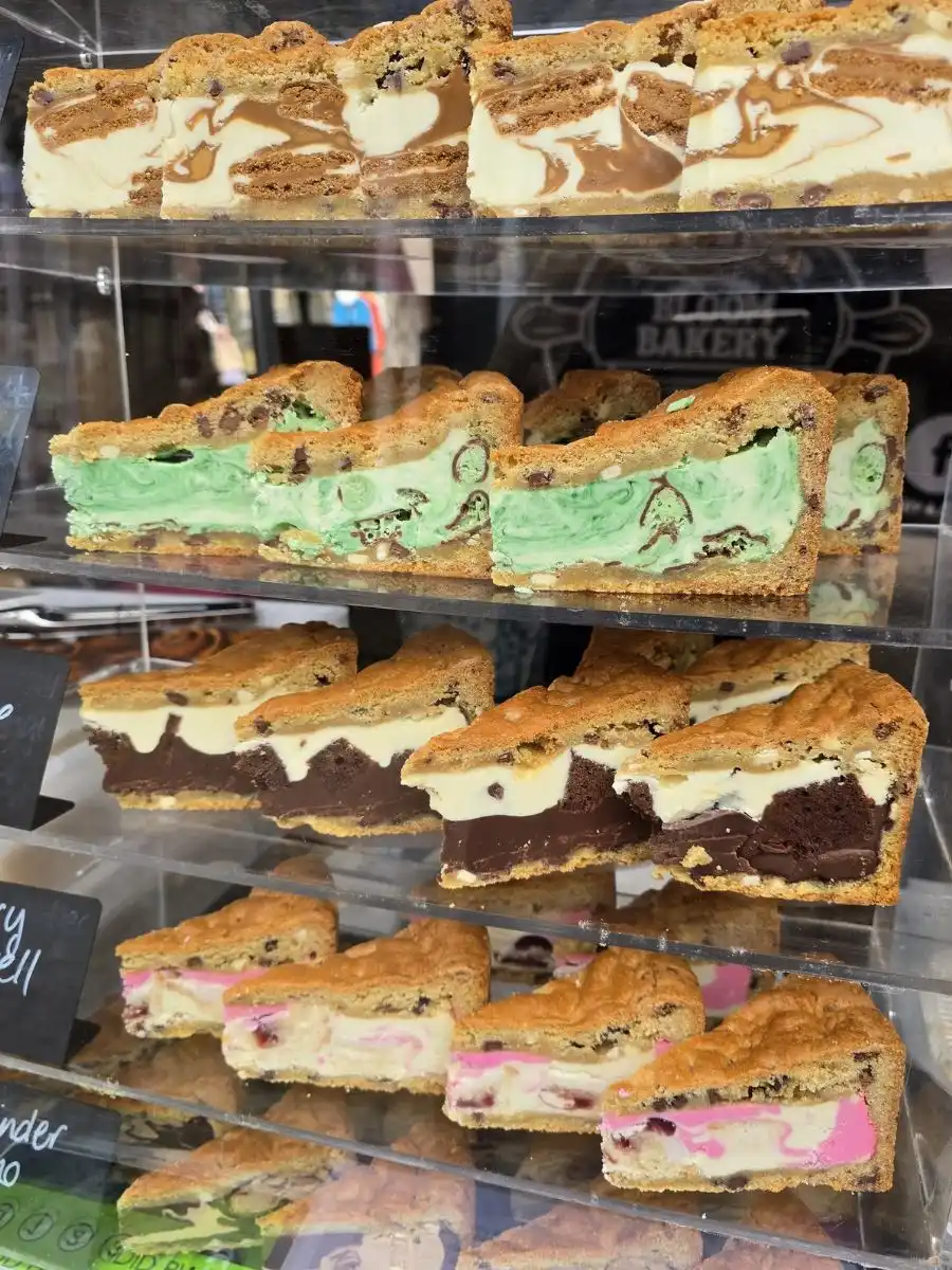 Five shelves of dessert bars in a display case, each with different flavours including chocolate, mint, and strawberry swirled between layers of cookie dough.