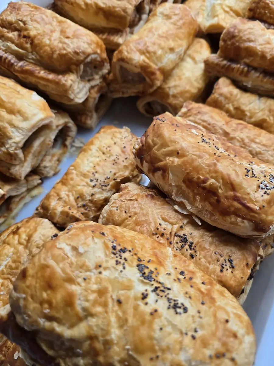 A tray filled with golden-brown puff pastry sausage rolls, some topped with poppy seeds.