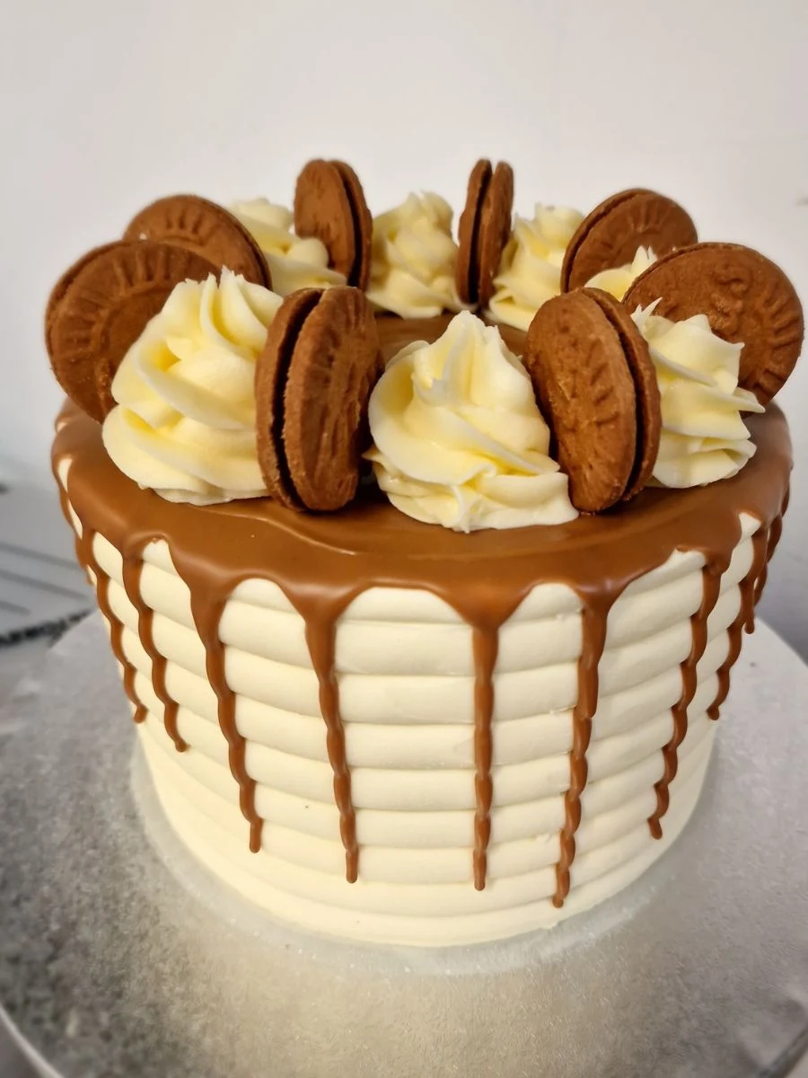 A layered cake with white frosting, caramel drip, and topped with swirls of icing and sandwich cookies.